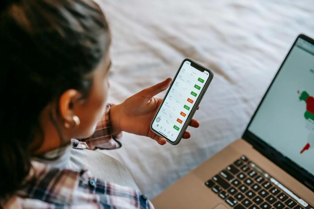 Crop ethnic analyst using trading application on smartphone on bed